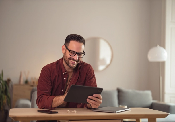 Photo of a man in glasses reading on a tablet while smiling