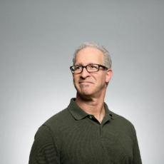 Photo of an old man in glasses with grey background smirking