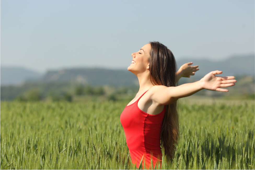 Woman breathing deep fresh air in a green wheat field wearing a red shirt