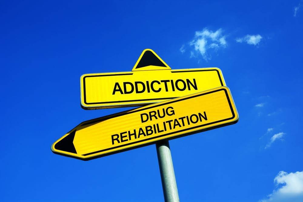 Addiction vs Drug Rehabilitation - Traffic sign with two options - appeal to overcome addictive substance abuse and dependence through detoxification, treatment, rehabilitation and abstinence