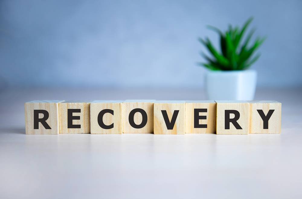 RECOVERY word concept written on wooden cubes lying on a light table and light background.